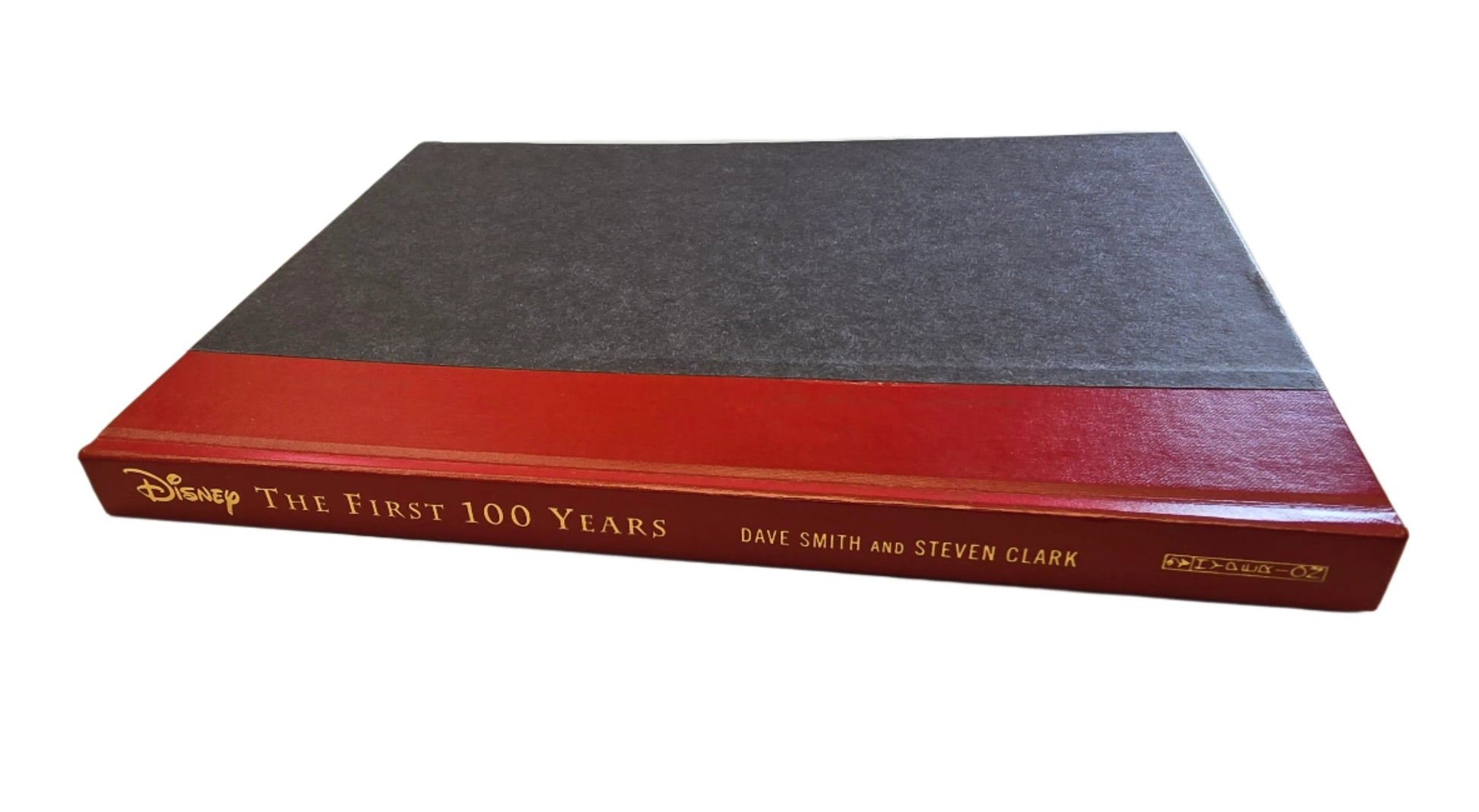 A black and red hardcover bound book with no dust jacket; Disney: The First 100 Years laying flat with the spine showcasing the title in gold letter